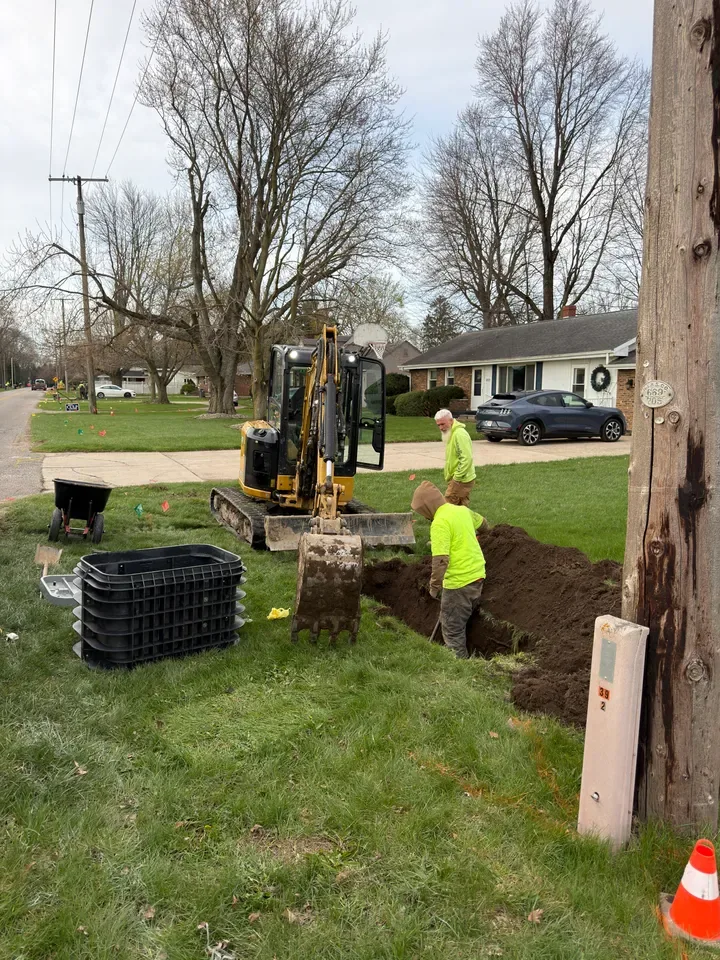 A Community Fiber crew digging along a residential street with a small excavator to lay fiber conduit
