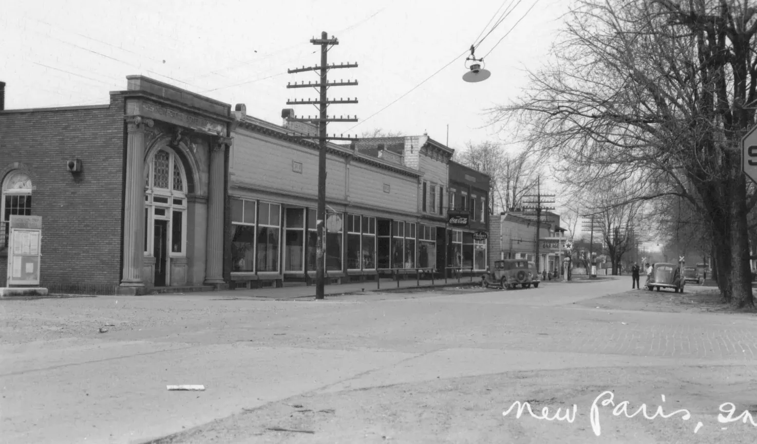 Downtown New Paris in the 1930s: the New Paris State Bank and a row of storefronts, with a telephone pole and its crossarms of lines standing at the curb