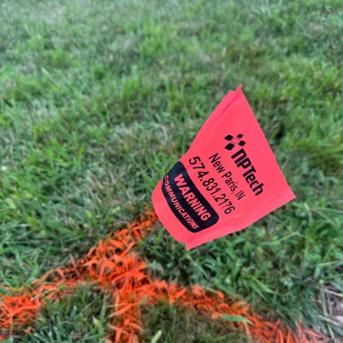 An NPTech utility marking flag in the grass before a dig